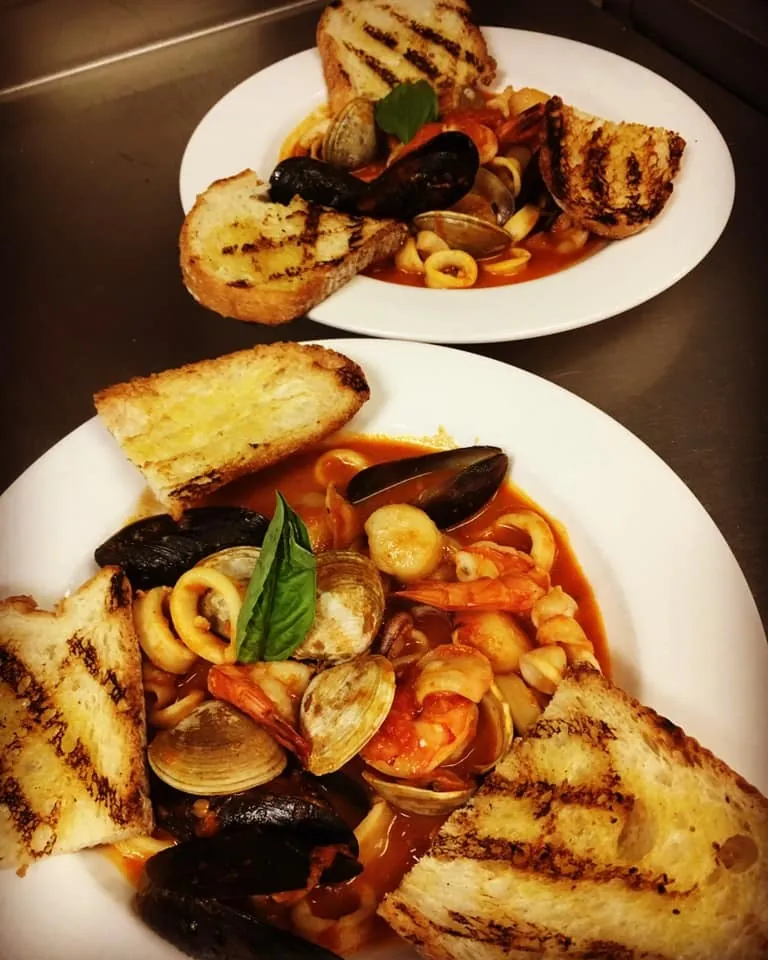 Two plates of mussels, clams and calamari in tomato broth with grilled bread