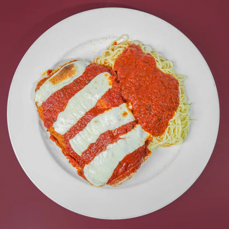 Eggplant Parmigiana with melted mozzarella beside spaghetti in tomato sauce