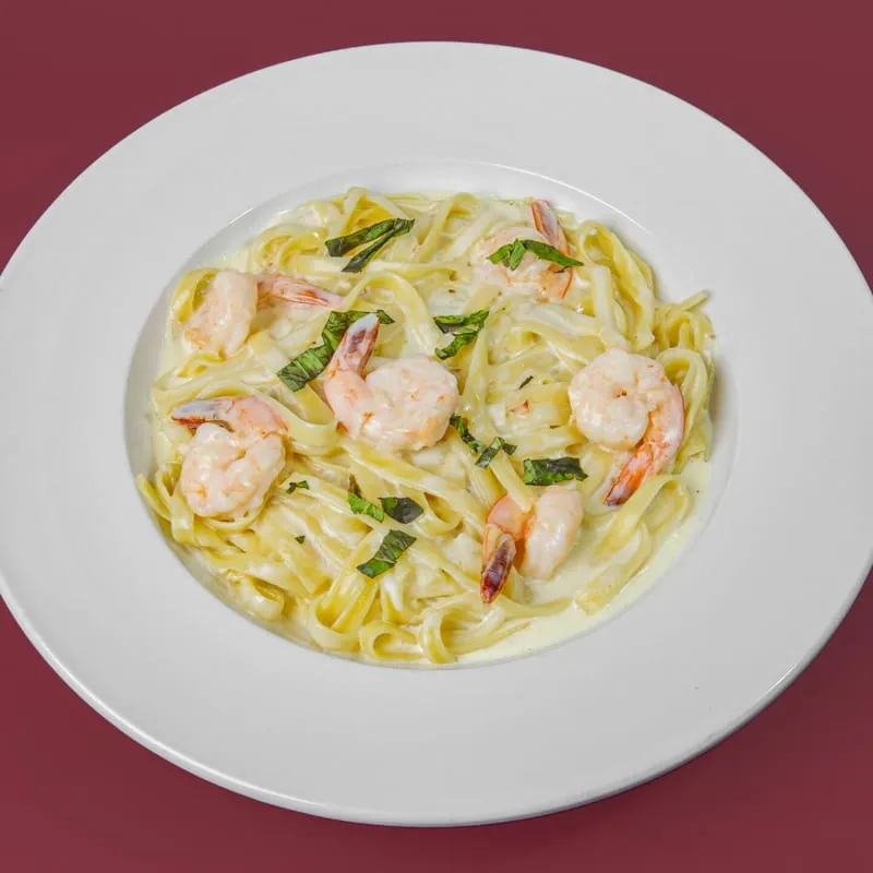 Fettuccine Alfredo topped with grilled shrimp and basil on a white plate